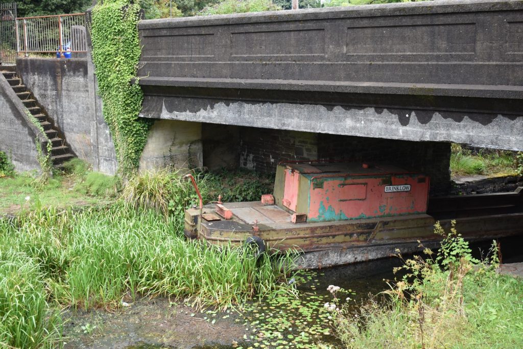The historic rusted metal barge sitting in inches of water under the bridge at Aberdulais.